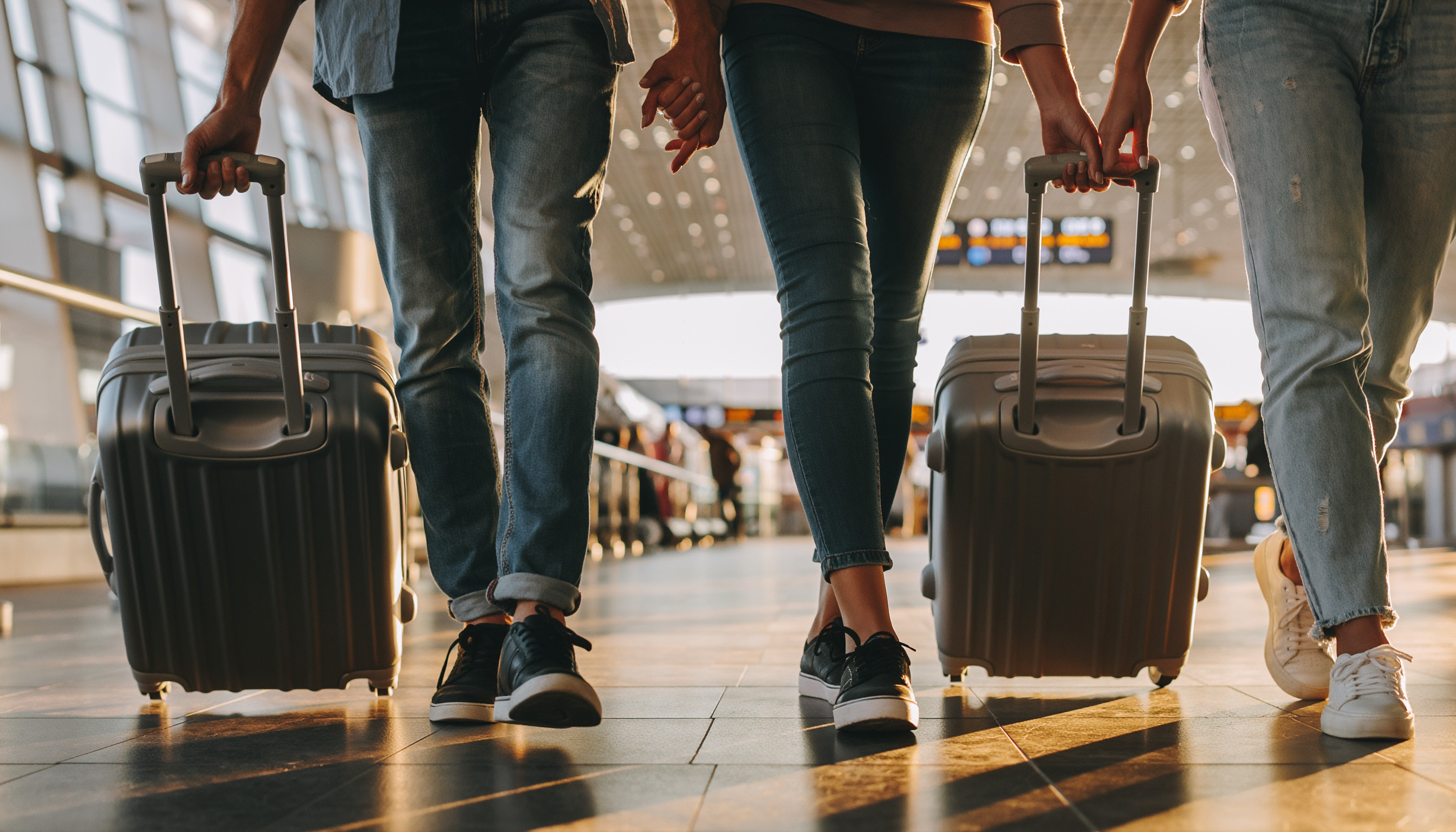 Two travelers wheeling their suitcases through a sunlit airport terminal